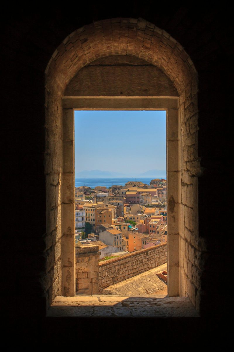 View of Korfu city and sea framed by an ancient stone arch in summer.